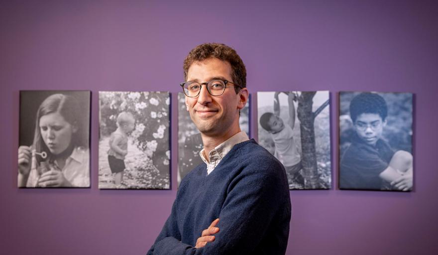 image of Schneider standing with arms crossed in front of purple wall and canvases