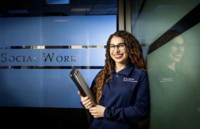 image of Scarlett Davalos standing at the School of Social Work, holding a folder