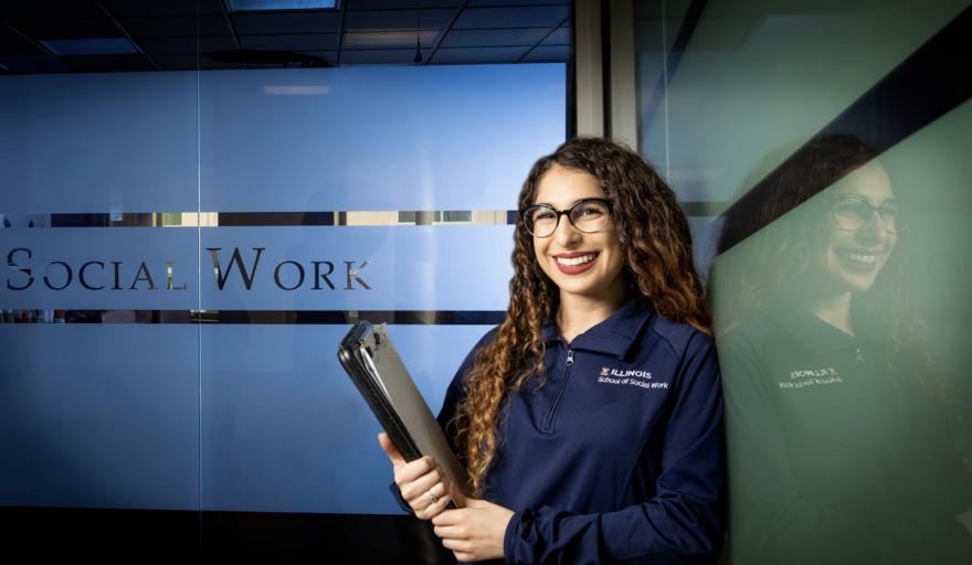 image of Scarlett Davalos standing at the School of Social Work, holding a folder