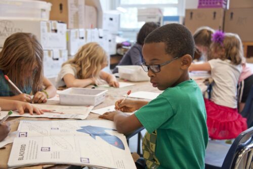 image of little boy seated in classroom and writing on paper