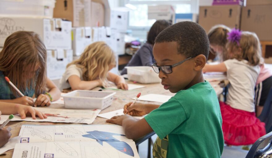 image of little boy seated in classroom and writing on paper