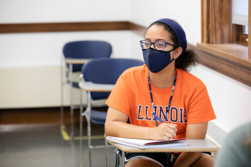 Female student with face covering takes notes in class.