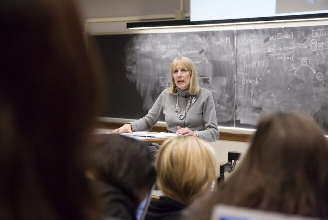 A female professor lectures in a classroom.