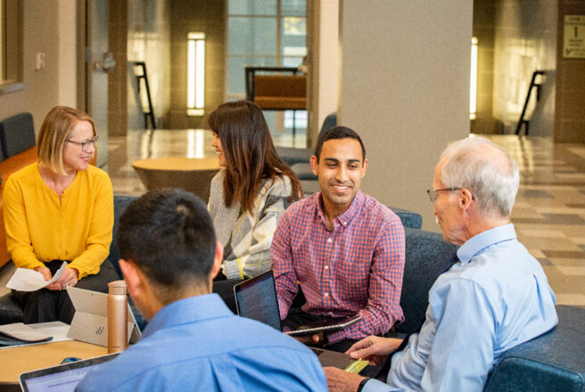 Students talking with laptops in study lounge.