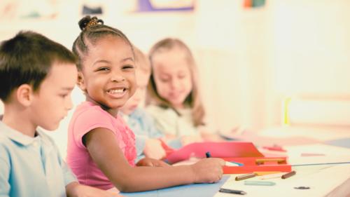 Three children smiling and drawing while sitting at a table