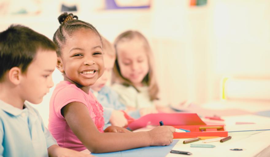 Three children smiling and drawing while sitting at a table