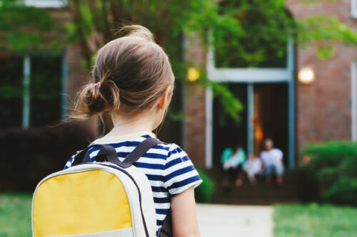 back of child returning home, wearing yellow backpack