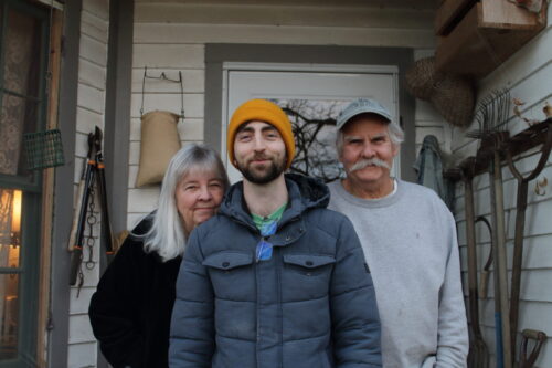 photo of Benjamin Pursley and an older couple at both his sides standing before a house front door